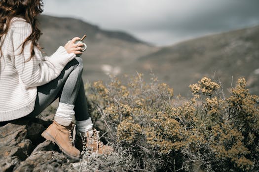 Young woman enjoying a peaceful coffee break in a beautiful mountain setting. Perfect for adventure and travel themes.