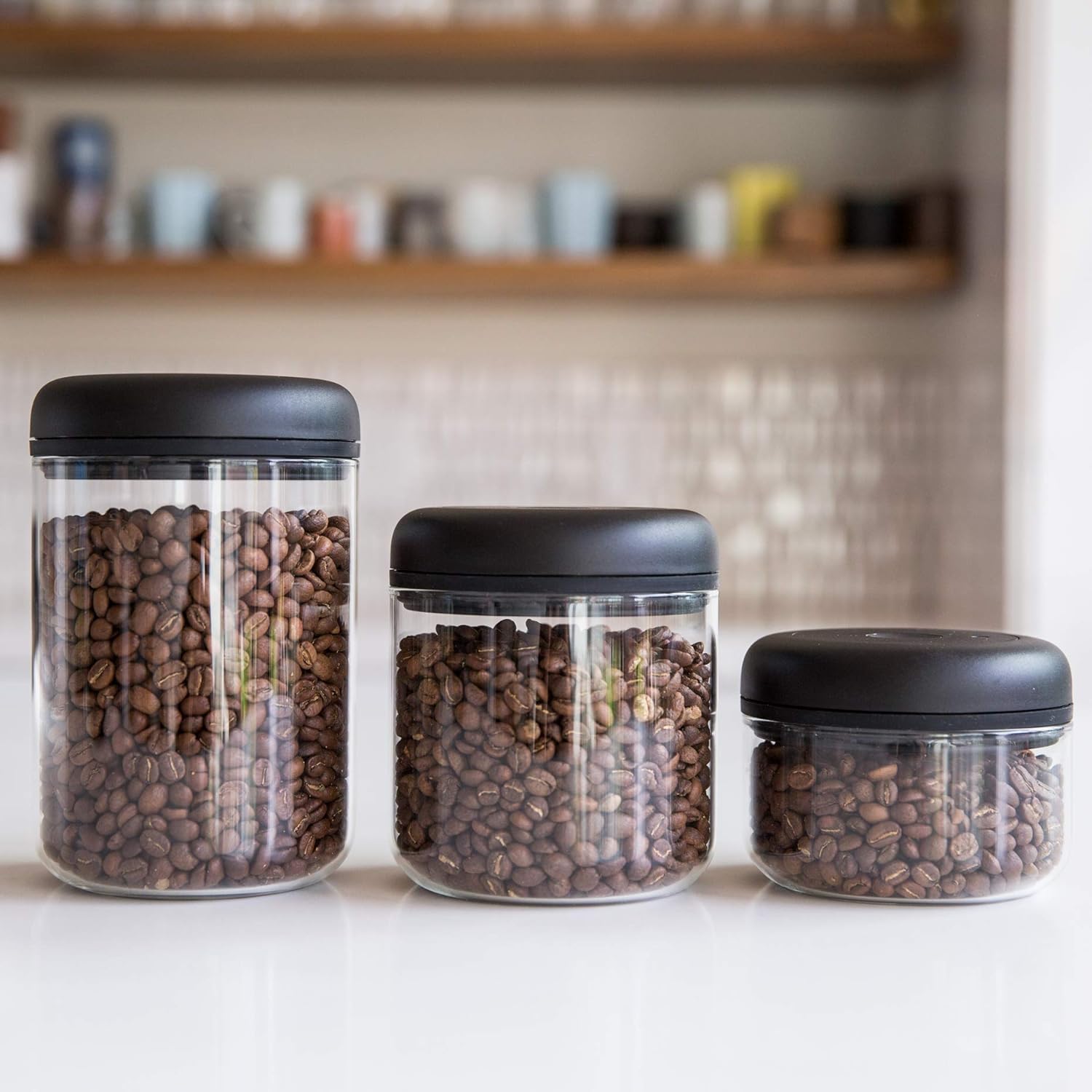 A set of three clear vacuum storage canisters holding coffee beans.