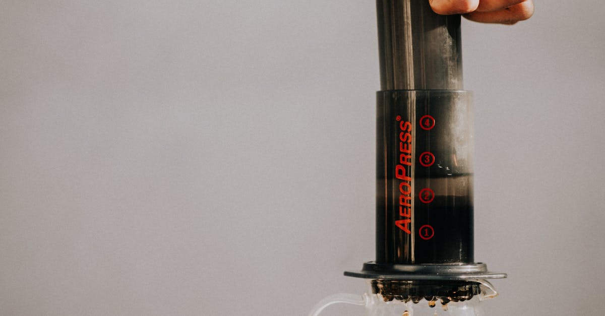A hand press brewing coffee using an Aeropress on a clear glass pitcher in a minimalist setting.
