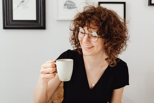 Caucasian woman with curly hair enjoying coffee at home, wearing eyeglasses.