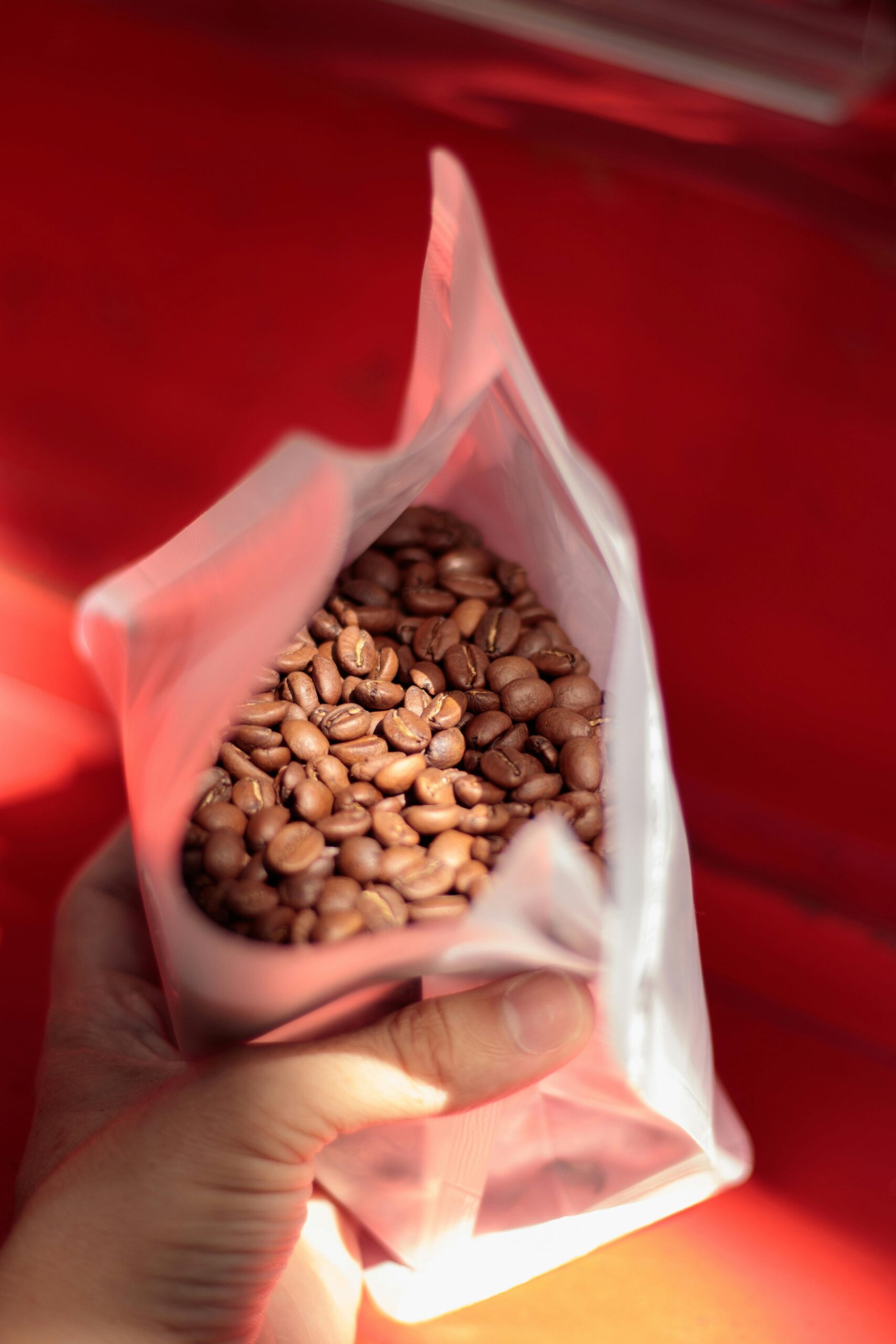 Close-up of a hand holding an opened bag of coffee beans over a vibrant red background.