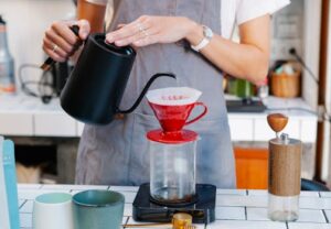 Barista using pour over method to prepare coffee in modern café setting.