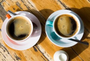 Top view of two black coffee cups on a sunny wooden table, Melbourne cafe vibe.